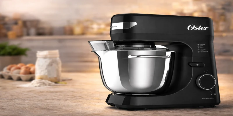 Batedeira planetária Oster preta com bowl inox e 12 velocidades sobre bancada de cozinha, ideal para massas, bolos e receitas de confeitaria caseira.